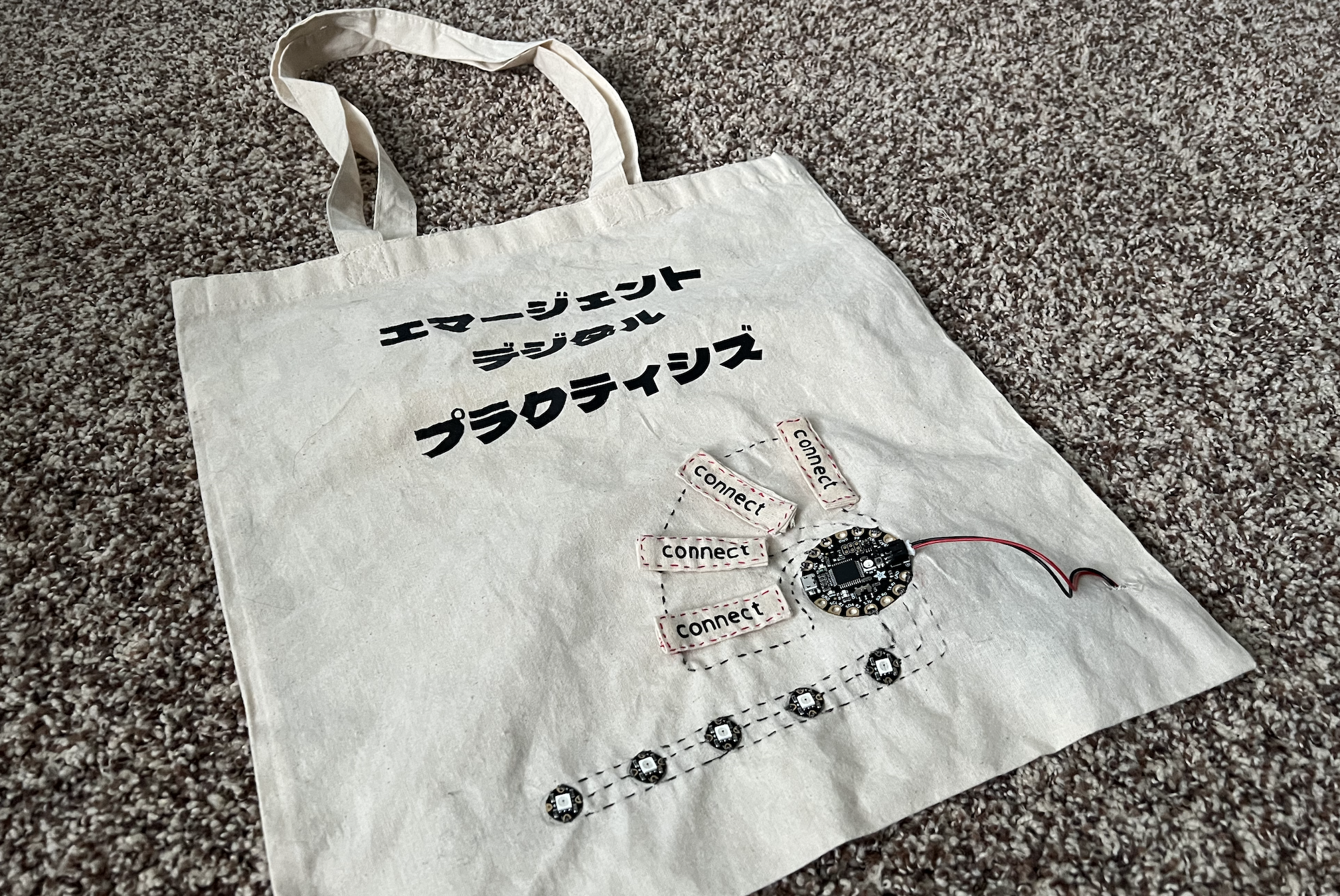 tote bag with circuits, LEDs and snaps. Emergent Digital Practices written in Japanese at the top